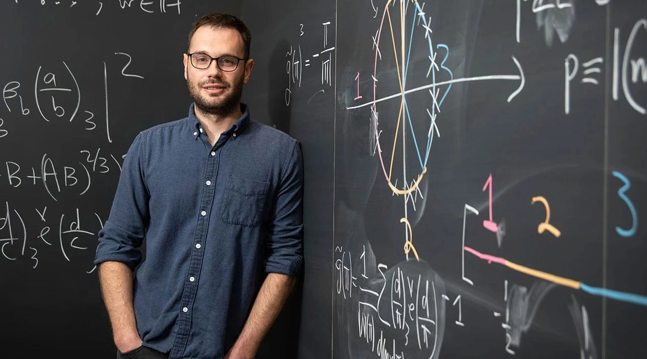 Man in glasses leaning against a blackboard.