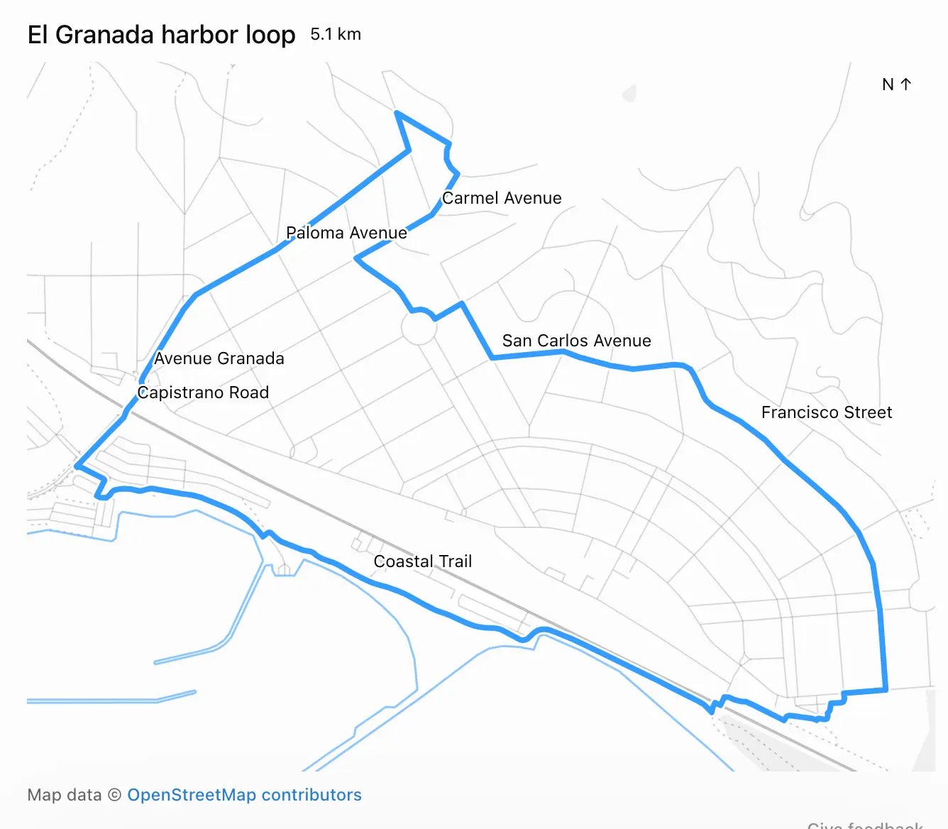 地图截图,显示在浅灰色街道图上叠加的蓝色路线。文字标注:El Granada 港口环线 5.1 公里。北方指示:↑(右上角)。沿路线的街道名称:Carmel 大道、Paloma 大道、San Carlos 大道、Avenue Granada、Capistrano 路、Francisco 街、Coastal 步道。路线从左下角的港口出发,沿 Avenue Granada 和 Paloma 大道向北至 Carmel 大道附近的北点,随后沿 San Carlos 大道向东,再沿 Francisco 街向南至最东端,最后沿海岸线旁的 Coastal 步道向西返回。页脚:地图数据 © OpenStreetMap 贡献者。反馈意见。